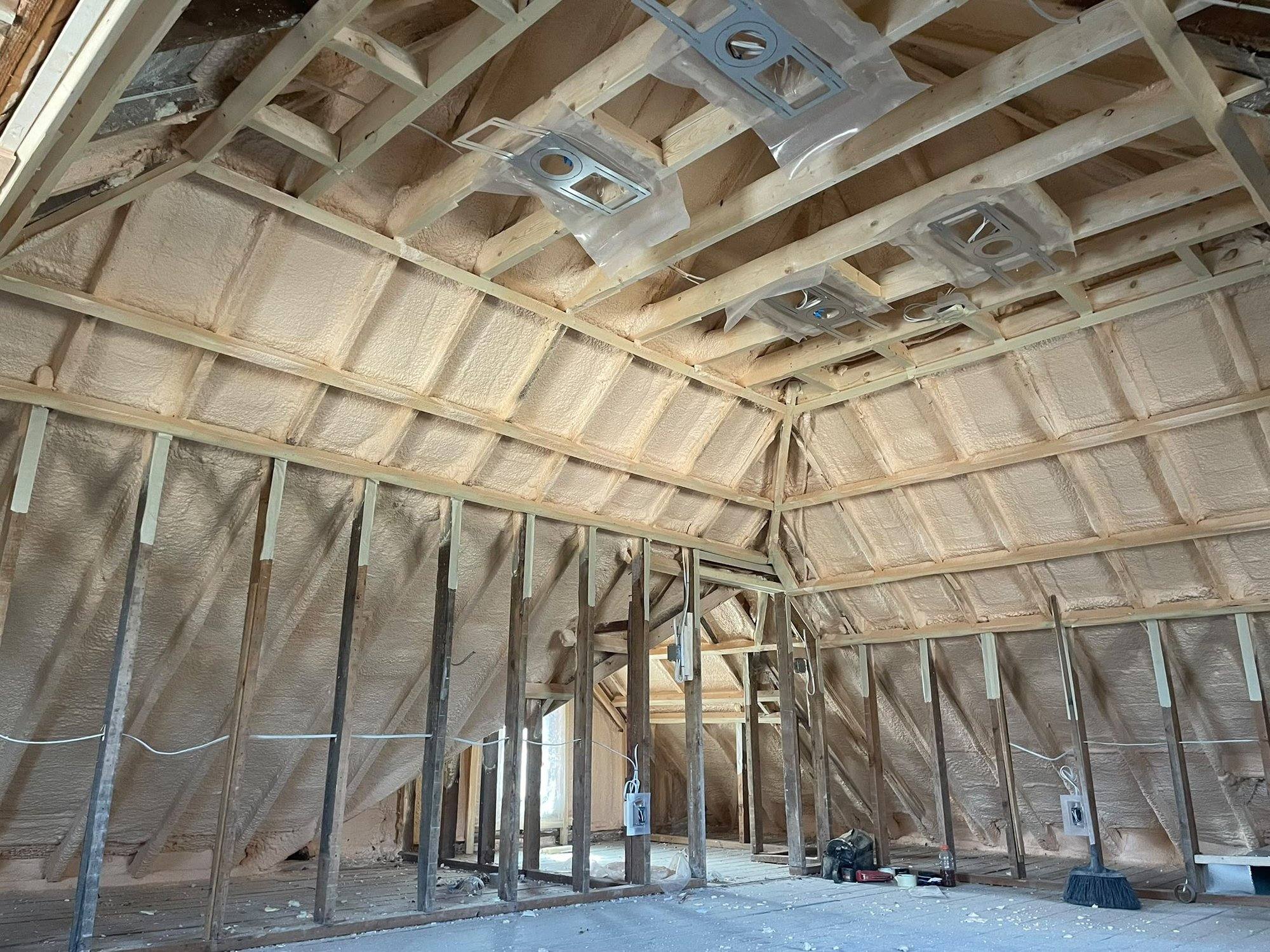 Interior of a steel-frame commercial building under construction with spray foam on the wall girts and HVAC ductwork installed overhead