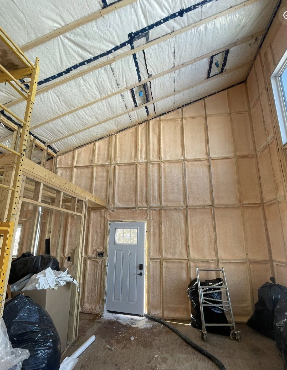 Tall interior wall fully spray foamed between studs under a vaulted poly-covered ceiling in a home under construction
