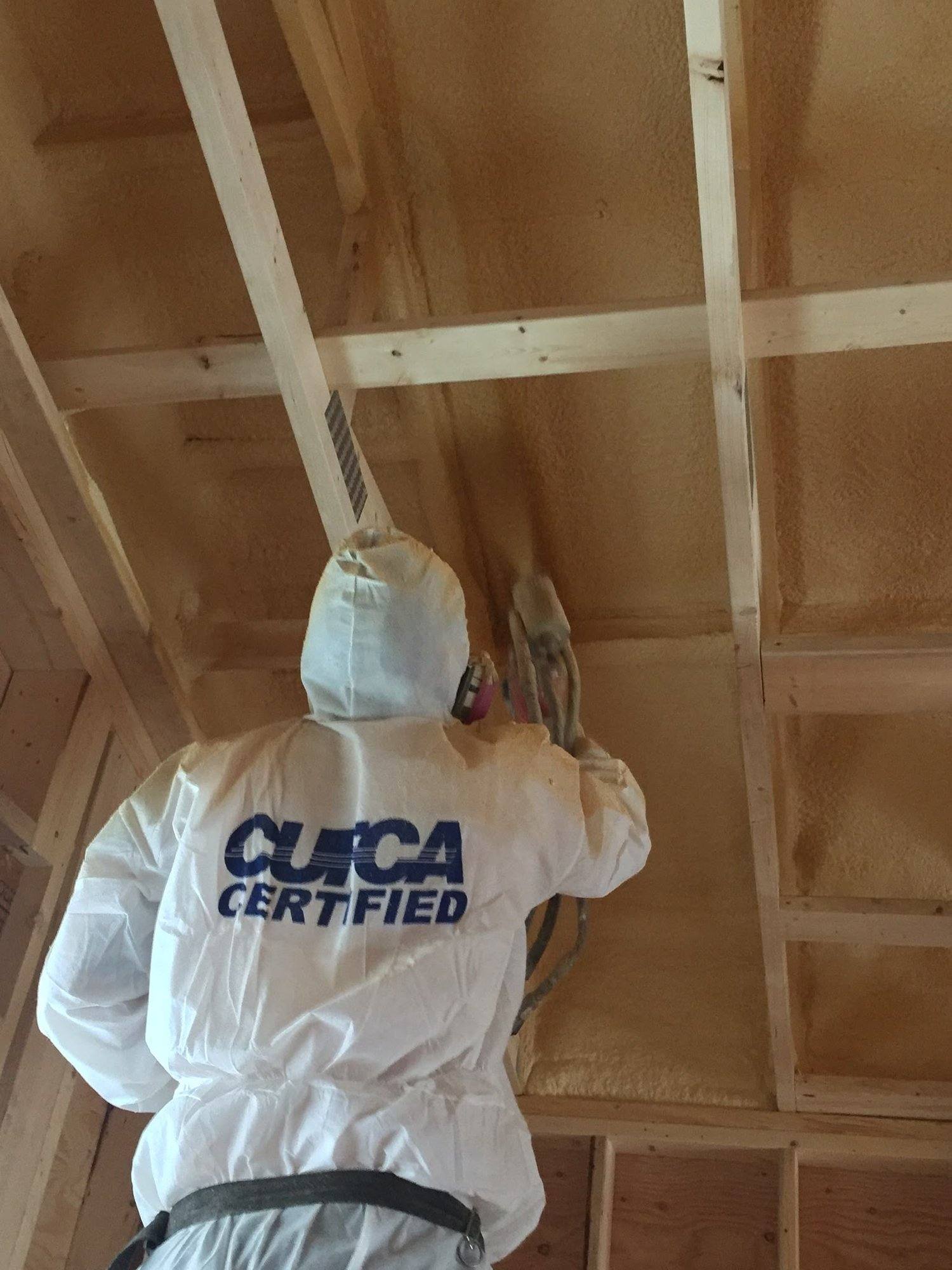 Ecologic installer in a CUFCA Certified coverall spray foaming an attic ceiling
