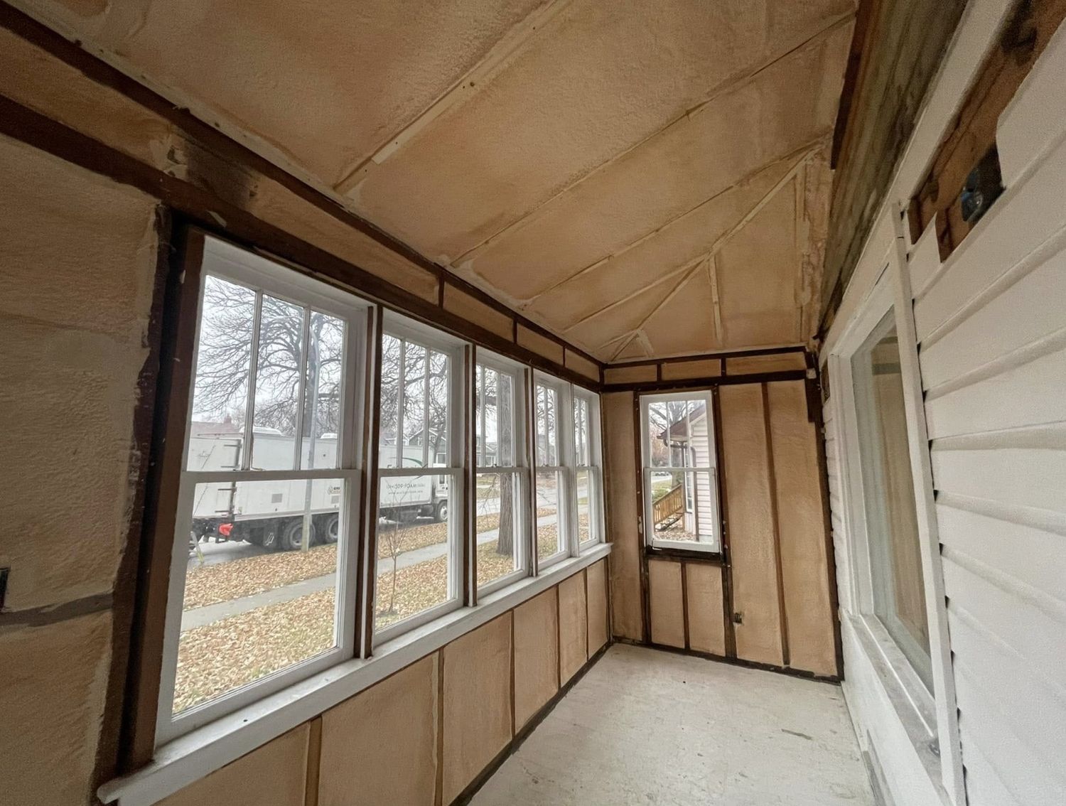 Enclosed porch with spray foamed walls and ceiling, insulation company truck visible through the windows