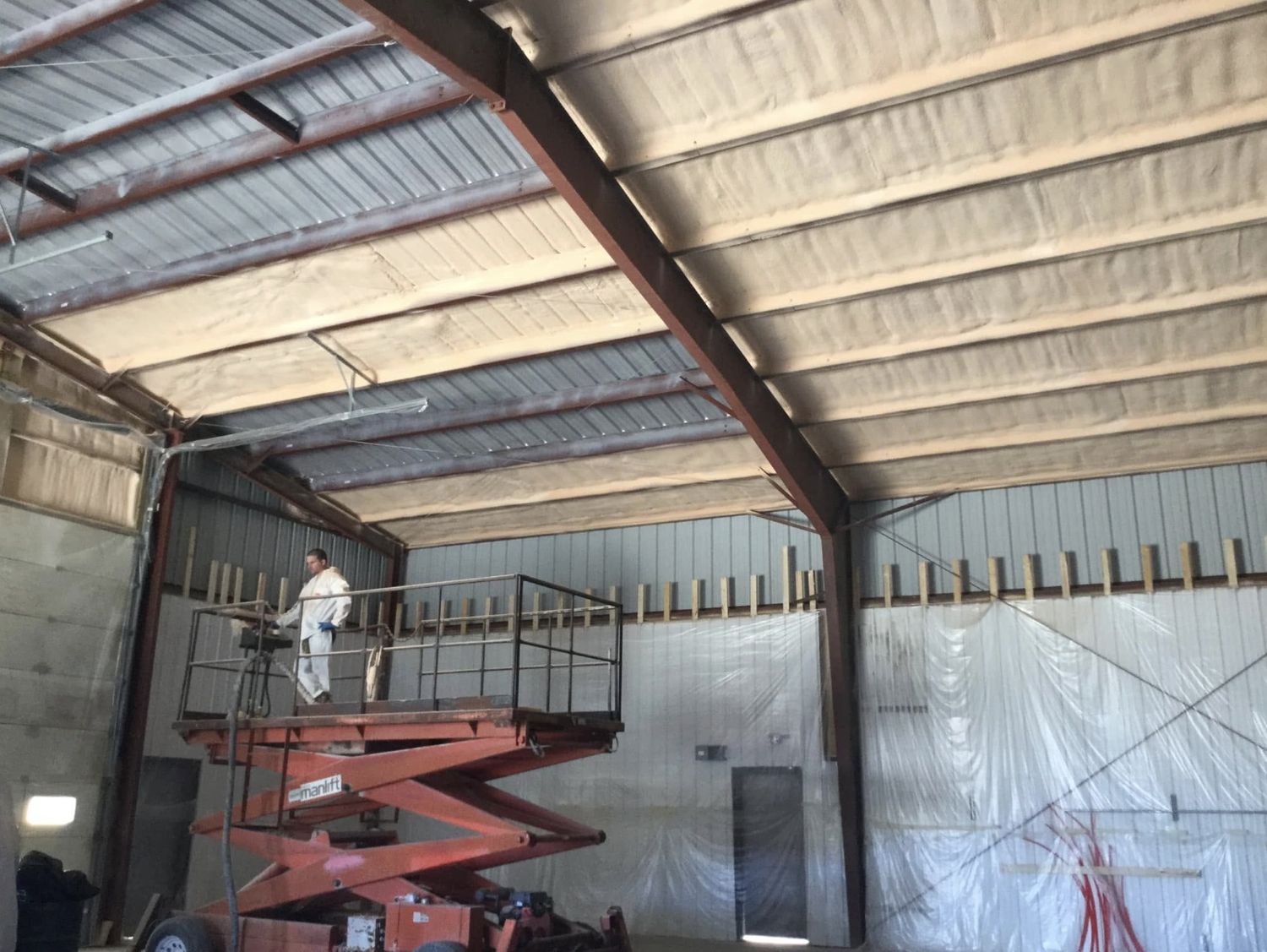 Spray foam being applied to a steel building roof from a scissor lift