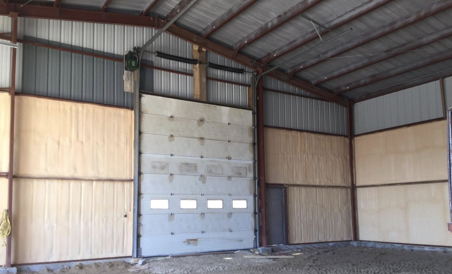 Steel shop building interior with spray foam applied to the walls between steel framing beside an overhead door